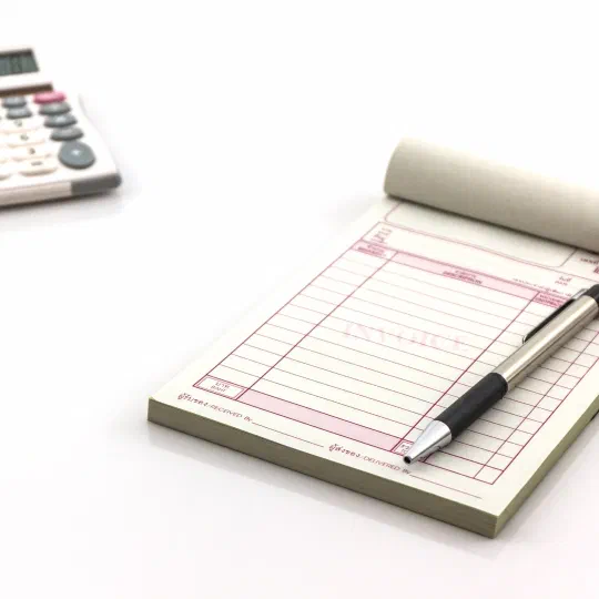 A carbonless invoice pad with a pen resting on it, beside a calculator