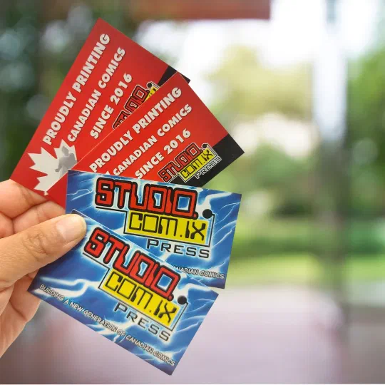 A hand holding Studiocomix Press business cards reading “Proudly printing Canadian comics since 2016”