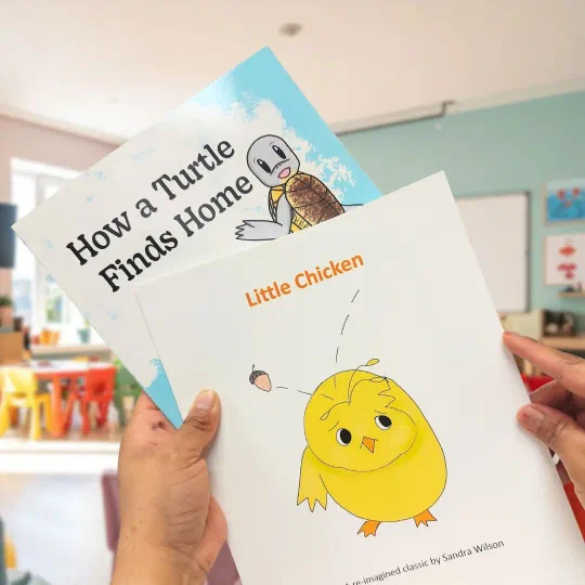 Two printed children’s picture books held up in a classroom