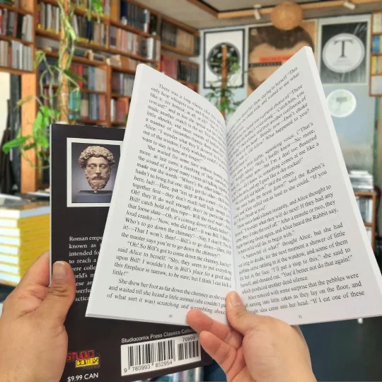 A paperback held open at a printed spread, with more copies stacked behind it